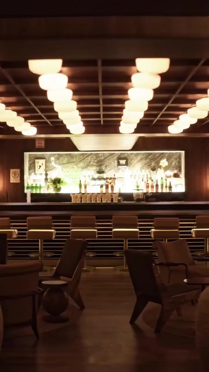 Salão do Le TT Speakeasy com teto de luminárias e bar ao fundo